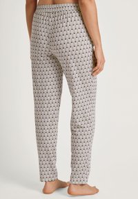 Patroon pyjamabroek met een witte basis, met een herhalend gekarteld ontwerp in groene en gouden tinten, een elastische tailleband en rechte pijpen.