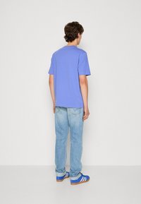 T-shirt s kratkimi rokavi v lavandulasti barvi, v kombinaciji s popljenjenimi modrimi kavbojkami in modrimi teniskami z belimi črtami. Preprost dizajn, sproščen kroj.
