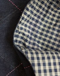 Denim tkanina s ružičastim šavovima, koja otkriva plavu i bijelu kariranu podlogu. Tekstura je glatka, s klasičnim kariranim uzorkom.