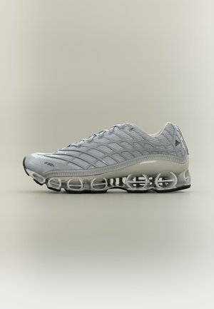 Grey athletic shoe with textured upper and transparent springy sole, designed for running or sports, shown in side profile on neutral background.