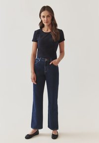 Camisa azul marino de manga corta combinada con pantalones vaqueros de pierna ancha de cintura alta en azul oscuro. Zapatos planos negros y textura suave con un diseño mínimo.