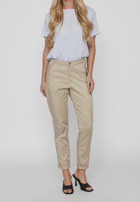 Chino beige con una vestibilità su misura, materiale in cotone, tasche frontali e orli arrotolati. Abbinati a un top azzurro a maniche corte e tacchi neri.