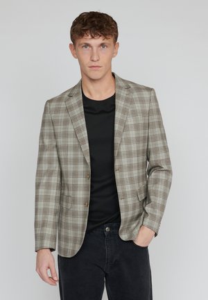 Jasnoszary blazer w brązowy wzór w kratę, z dwoma guzikami, z wyłogami klapami i przednimi kieszeniami, noszony na czarnej koszulce i ciemnych dżinsach.