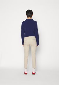 Marineblauer Pullover, beigefarbene Slim-Fit-Hosen und mehrfarbige Sandalen. Das Design zeichnet sich durch eine kurze, figurbetonte Silhouette mit gemusterten Akzenten auf dem Schuhwerk aus.