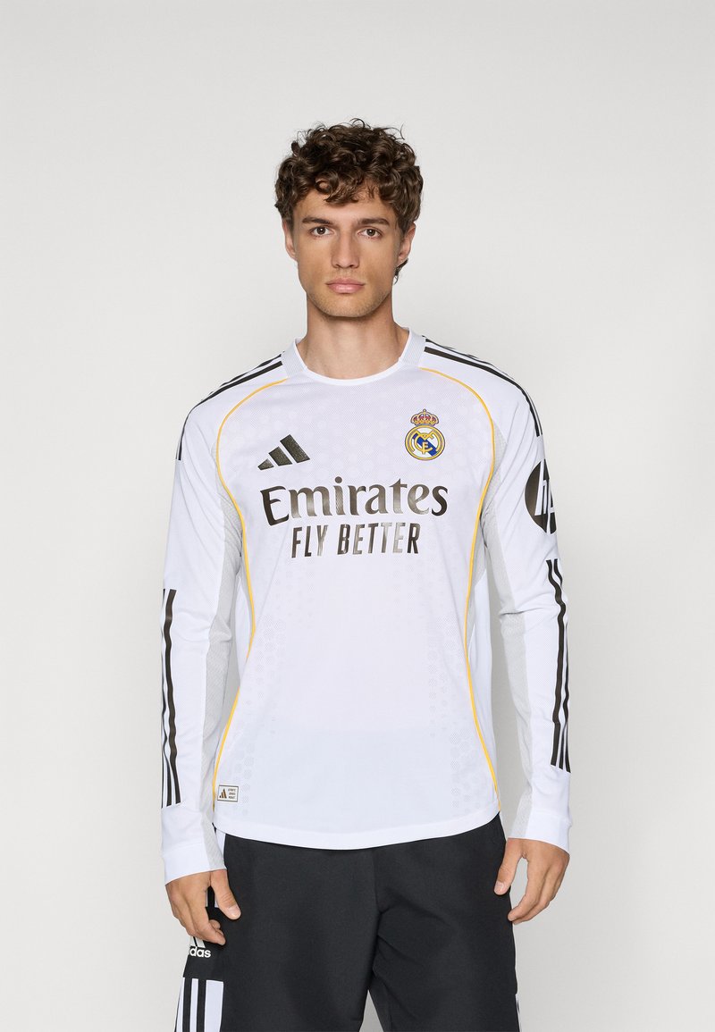 Hvid langærmet trøje med gule detaljer, sorte striber på ærmerne, har "Emirates Fly Better" logo og Real Madrid våbenskjold.