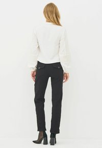 Hvid langærmet bluse med stribede detaljer og en høj halsudskæring, kombineret med sorte smalle bukser med knappede baglommer.