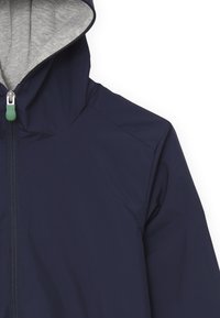 Giacca antipioggia blu marina con rivestimento grigio del cappuccio, zip frontale con un manico verde e tessuto liscio, resistente all'acqua.