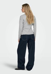 Sivi pulover z dolgimi rokavi, kombiniran z temno modrimi kavbojkami širokih nogavic. Obleka ima preprost dizajn in gladke teksture.