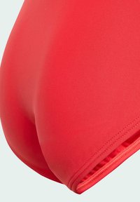 Červené jednodílné plavky z hladkého, elastického materiálu. Mají bezšvový design a kontrastní prošívání podél okrajů.