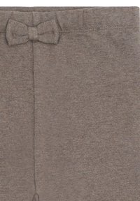 Sezione di abbigliamento in tessuto lavorato a maglia marrone con un piccolo dettagliato fiocco in tessuto abbinato vicino al bordo superiore.