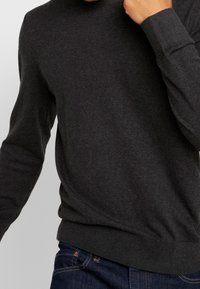 Maglione grigio realizzato in un morbido tessuto a maglia testurizzata. Caratterizzato da maniche lunghe, scollo rotondo e polsini e orlo a coste. Indossato con jeans.