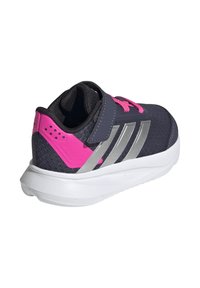 Zapatilla deportiva de un oscuro color navy con acentos en rosa, rayas plateadas y material texturizado. Presenta una correa de gancho y bucle y una suela blanca acolchada.