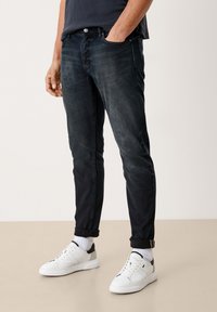 Jeans de denim oscuro ajustados con deslavado, cinco bolsillos y puños enrollados. Llevados con zapatillas blancas y calcetines blancos de canalé.