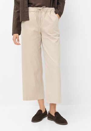 Beige bredbenskorte bukser med snøre i taljen, båret med mørkebrune loafers og en mørk langærmet top.