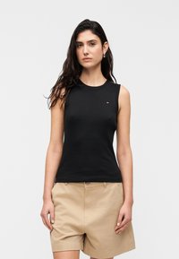 Μαύρο αμάνικο τοπ σε εφαρμοστή γραμμή, κατασκευασμένο από απαλό ύφασμα. Διαθέτει μικρή διακριτική λογότυπη λεπτομέρεια στο αριστερό στήθος. Φοριέται με μπεζ σόρτς.