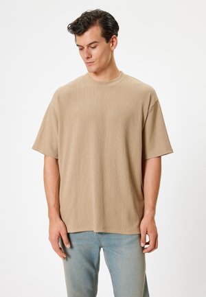 Camiseta beige de manga corta en tejido texturizado con escote redondo. Combinada con jeans de mezclilla azul claro. Diseño simple y relajado.
