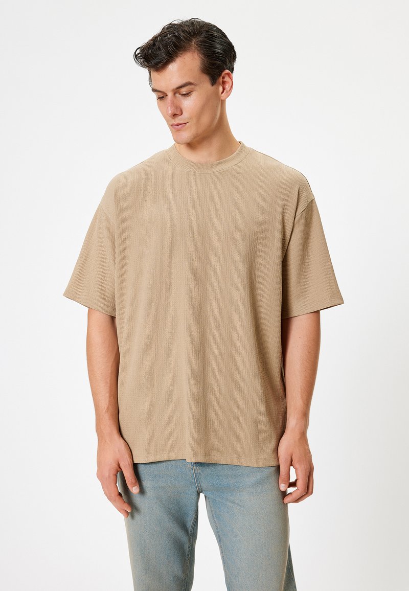 Beige kortærmet t-shirt i tekstureret stof med rund hals. Kombineret med lyseblå denim jeans. Enkel, afslappet design.