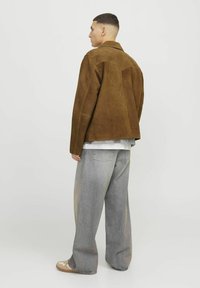 Brown suede jacket with a relaxed fit, featuring a structured collar and shoulder accents, paired with loose-fitting, light denim jeans.