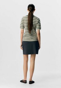 Top a righe in maglia beige e olivo, abbinato a una gonna grigio scuro, completato con scarpe nere in rete. Capelli legati, vista da dietro.