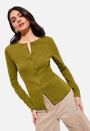 Olijfgroene geribbelde cardigan met lange mouwen, een ronde halslijn en een knoopsluiting aan de voorkant, gecombineerd met lichtbeige broek.