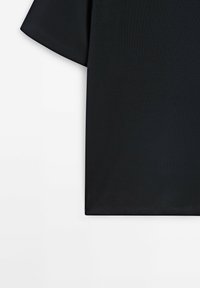 Zwarte t-shirt met korte mouwen en zichtbare stiksels op de mouwen en zoom, plat gelegd op een witte achtergrond.