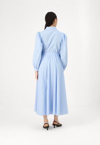 Ανοιχτό μπλε μακρύ φόρεμα με φουσκωτά μανίκια, ελαστική μέση και φαρδιά φούστα. Φοριέται με μαύρες ψηλές γόβες. Απλό και κομψό σχέδιο.