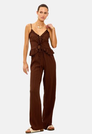 Combinaison marron à côtes avec taille peplum, bretelles spaghetti réglables et détail de nœud à l'avant ; assortie à des sandales légères.