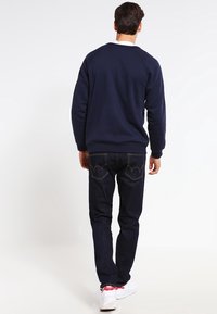 Marinsvett med raglanärmar, kombinerad med mörk denimjeans som har tydliga bakfickor och vita sneakers.