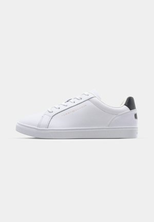 Zapatilla de cuero blanca con un acabado liso, diseño con cordones, detalle del logo en dorado metálico y un acento en negro contrastante en el talón.