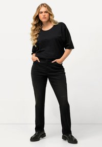 Camiseta negra de manga corta combinada con vaqueros negros de tiro alto. La modelo lleva zapatos negros de suela gruesa. Diseño simple y moderno con líneas limpias.