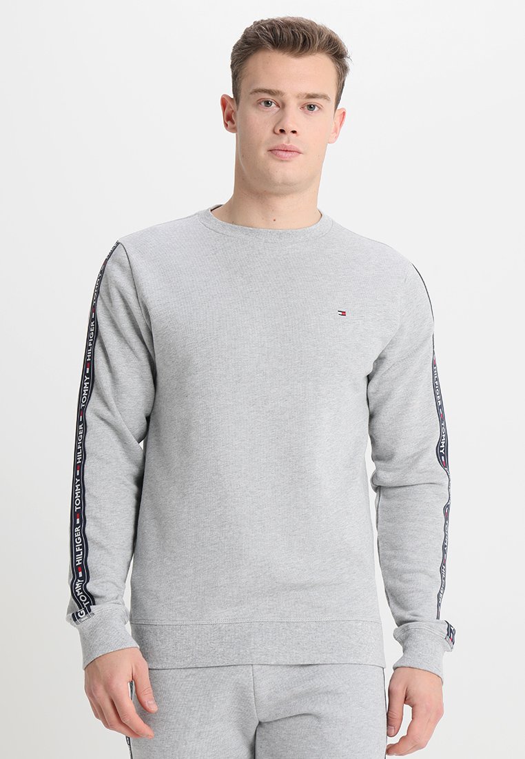 Sweatshirt en coton gris avec un col rond, des poignets côtelés et des bandes latérales imprimées de logo en rouge et bleu. Coupe régulière et texture douce.
