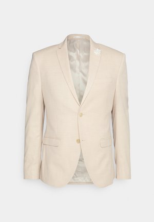 Blazer in lino beige con rever a punta, due tasche frontali, due bottoni e una spilla floreale sul rever. Fodera interna liscia e vestibilità su misura.