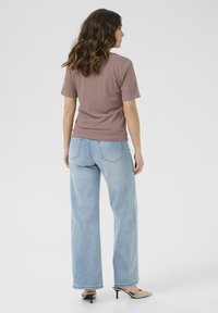 Top corto de manga corta de color marrón claro con textura acanalada, combinado con unos pantalones vaqueros de pierna ancha de color azul claro, que presentan un corte relajado y detalles de costura sutiles.