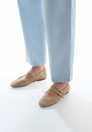 Ballerines en daim beige avec un bout arrondi, dotées de deux straps réglables et d'un petit talon, associées à un pantalon bleu clair.