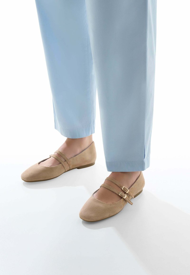 Ballerines en daim beige avec un bout arrondi, dotées de deux straps réglables et d'un petit talon, associées à un pantalon bleu clair.