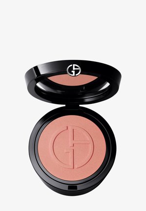 Rund blush-kompakt med en glanset svart ytre. Inni er det en myk ferskenfarget rouge med et subtilt preget logomønster. Glatt, matt tekstur.