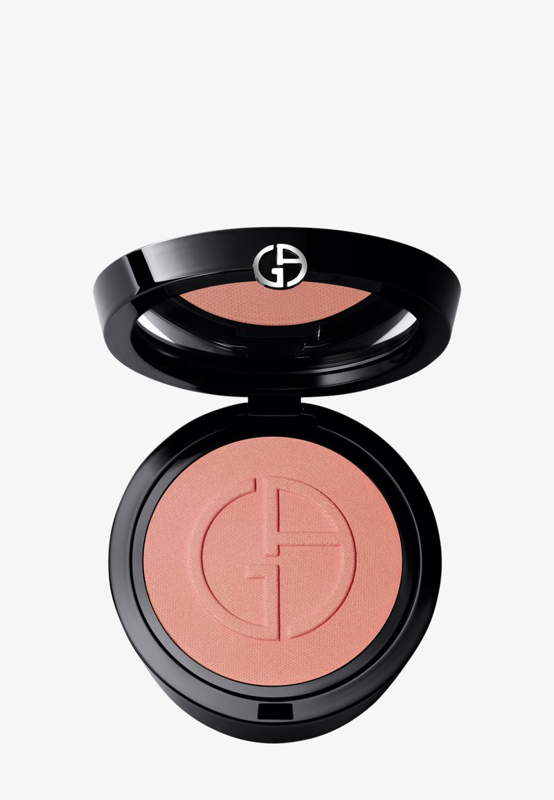 Rund blush-kompakt med en glanset svart ytre. Inni er det en myk ferskenfarget rouge med et subtilt preget logomønster. Glatt, matt tekstur.