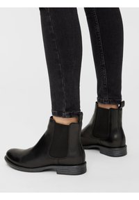 Schwarze Leder-Ankle-Boots mit elastischen Seitenteilen und einem niedrigen Blockabsatz, kombiniert mit schwarzen Skinny-Jeans, die eine elegante Silhouette zeigen.