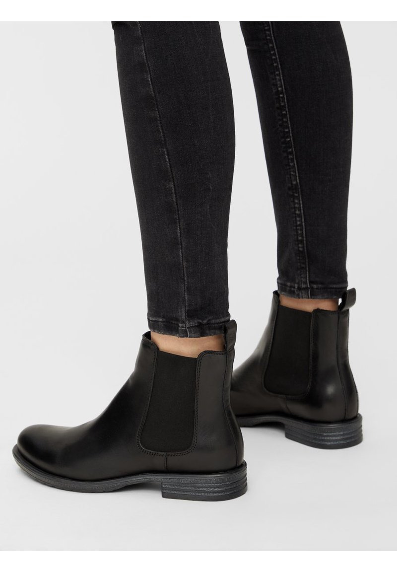 Schwarze Leder-Ankle-Boots mit elastischen Seitenteilen und einem niedrigen Blockabsatz, kombiniert mit schwarzen Skinny-Jeans, die eine elegante Silhouette zeigen.