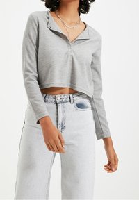 Graues, tailliertes Langarmoberteil mit Kragen, Knopfdetails und geripptem Material, kombiniert mit hellen, hochgeschnittenen Jeans.