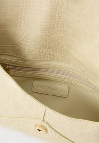 Κρεμ γυναικεία τσάντα με υφή κροκοδείλου, διαθέτει τσέπη με φερμουάρ και κλείσιμο με κουμπί σε χρυσή απόχρωση. Το εσωτερικό έχει λείο φινίρισμα.