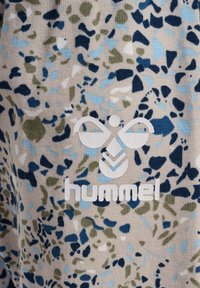 Blommönstrad tyg i krämfärg med blå, grön och marinblå former. Innehåller en vit "hummel"-logotyp och ribbad textur.