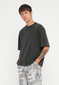 Dark gray oversized t-shirt with short sleeves, ribbed neckline, and subtle stitching details, paired with patterned light trousers.