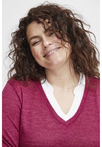 Burgundy stickad tröja med V-ringning, lagd över en vit skjortkrage. Texturen verkar mjuk och har en avslappnad passform.