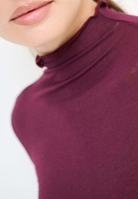 Maglione a collo alto color bordeaux con una trama liscia, caratterizzato da un piccolo dettaglio con bottone al collo.