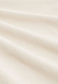 Gros plan d'un tissu doux et lisse de couleur crème avec des plis doux et une texture subtile.