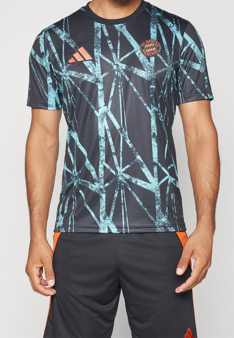 Musta urheilupaita, jossa on sininen abstrakti geometrinen kuvio, pyöreä kaulus, lyhyet hihat ja FC Bayern Münchenin logo rinnassa.