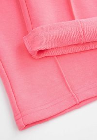 Różowa bawełniana tkanina o gładkiej fakturze, z podwiniętymi mankietami i starannym ściegem, prezentująca prosty wzór i żywy kolor.