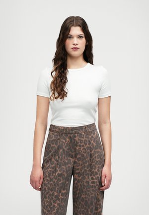 Camisa justa de manga curta branca combinada com calças castanhas de cintura alta com padrão de leopardo; textura suave, ajuste sob medida.