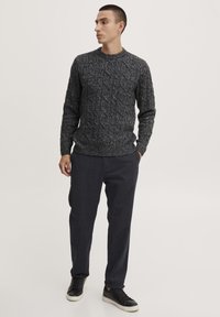 Tamsiai pilkas tekstūruotas megztinis su kabelinės pynės raštu, derinamas su tamsiai mėlynomis kelnėmis ir juodais sportbačiais. Paprastas apvalus iškirpimas ir raukiniai ant rankovių.